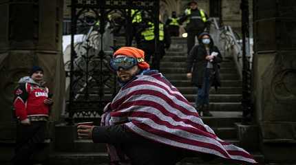 man wearing an American flag walks by police guarding the Canadian parliament building