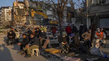 People sit next to a destroyed house