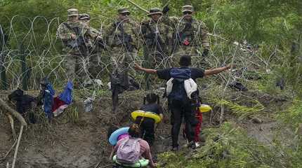 migrant gestures to Texas National Guards standing behind razor wire 