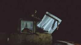 worker moves debris on top of damaged house